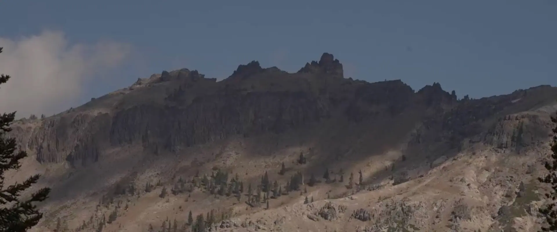 View of the rocky Castle Peak ridgeline with sparse trees beneath a blue sky.
